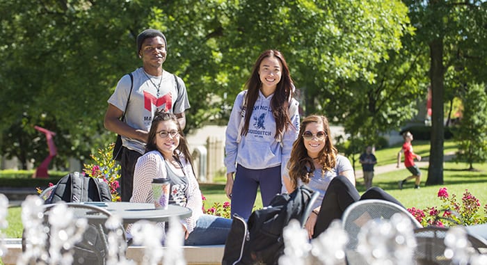 4 diverse students smiling at the camera on a sunny day