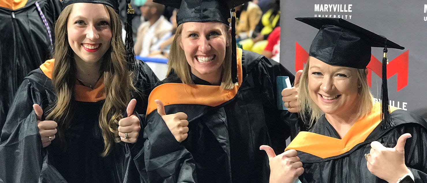 three students who give a thumbs up sign during graduation ceremony