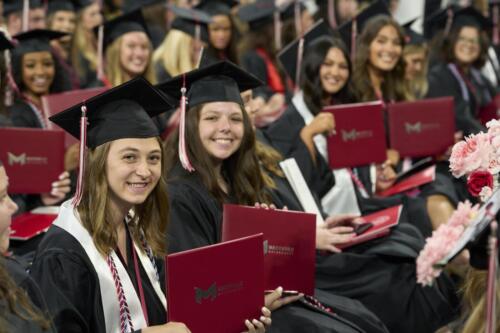 students holding diploma book during commencement