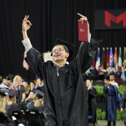 student raising arms in air after receiving diploma