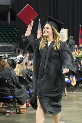 student waving to friends and family after receiving diploma