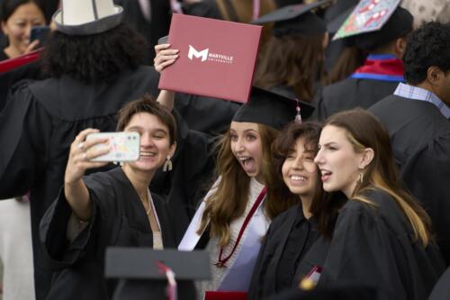 one student taking a selfie with three other graduates