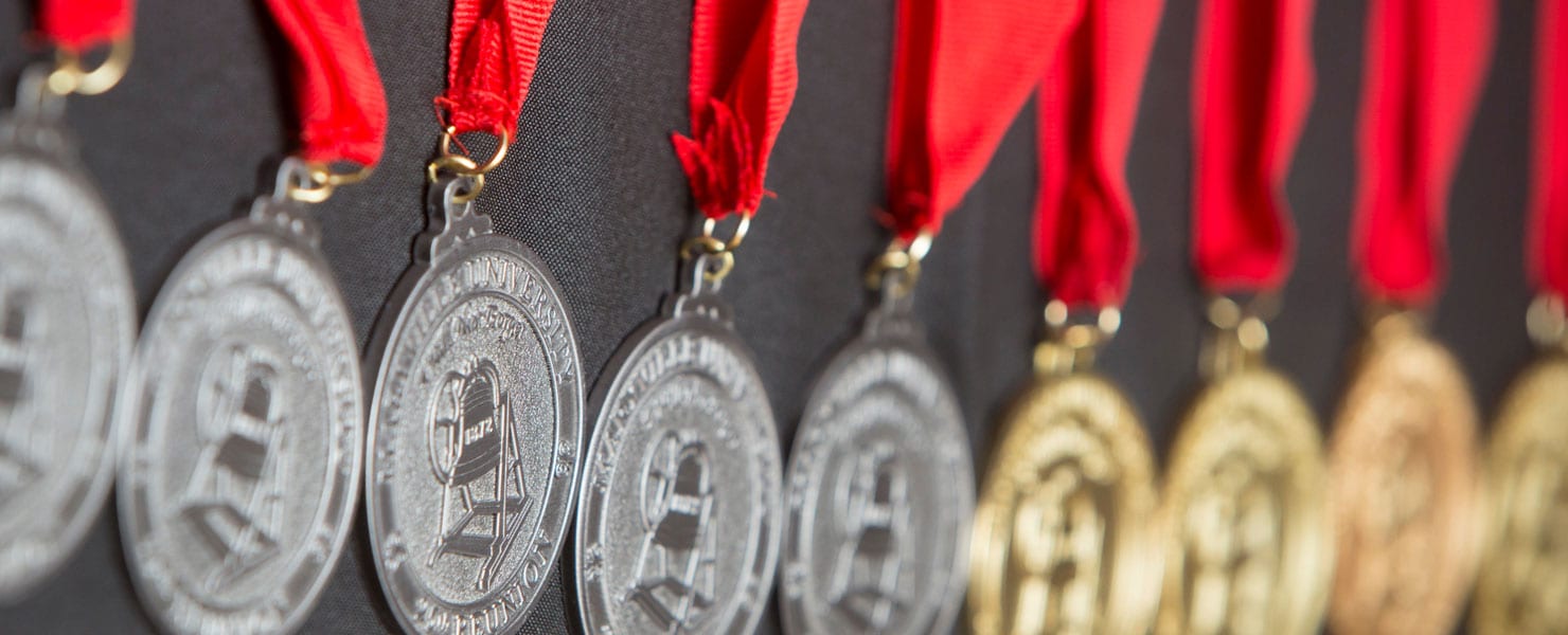 Medals with ribbons hanging side by side on a wall.