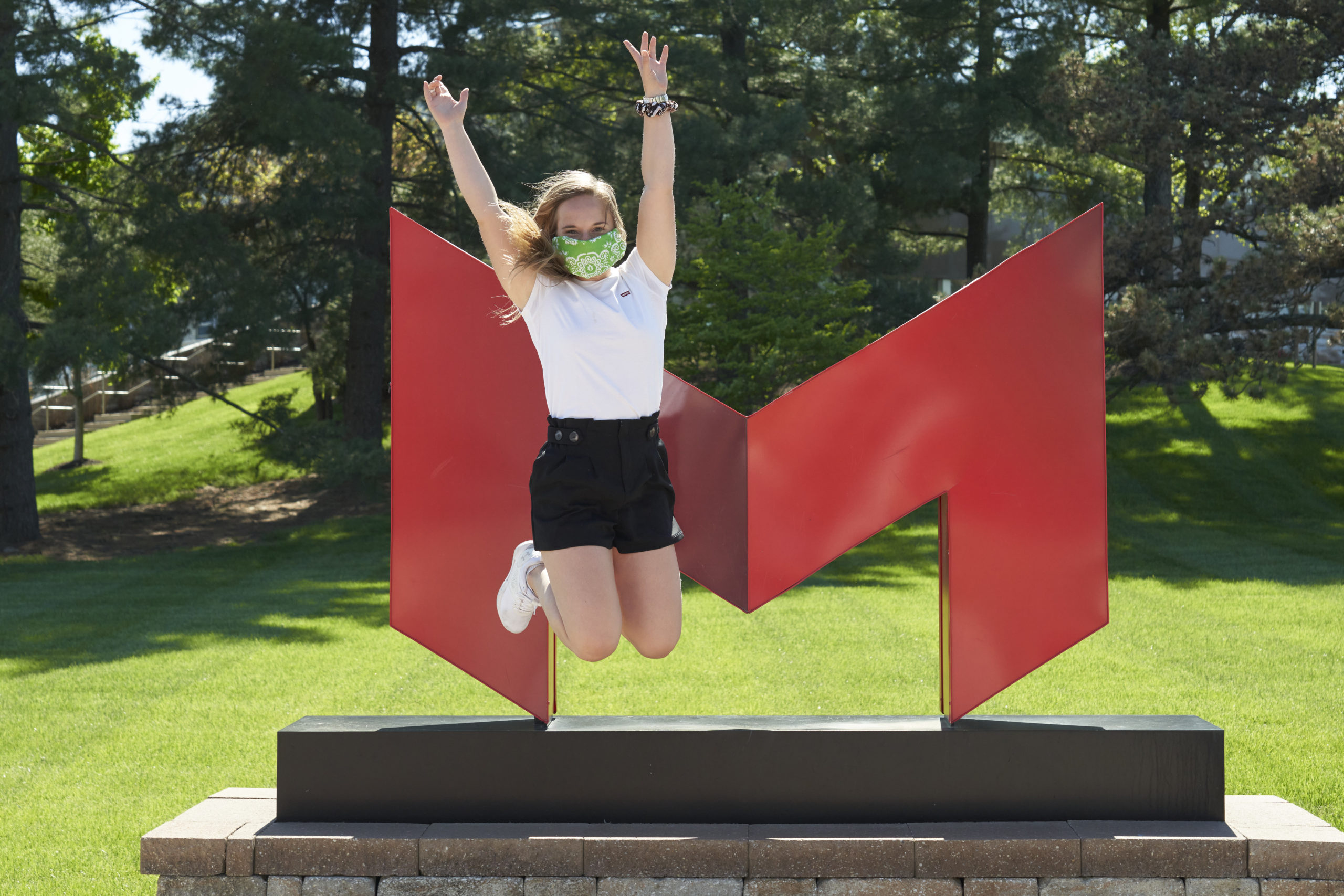 student with mask on jumping in front of Saints M